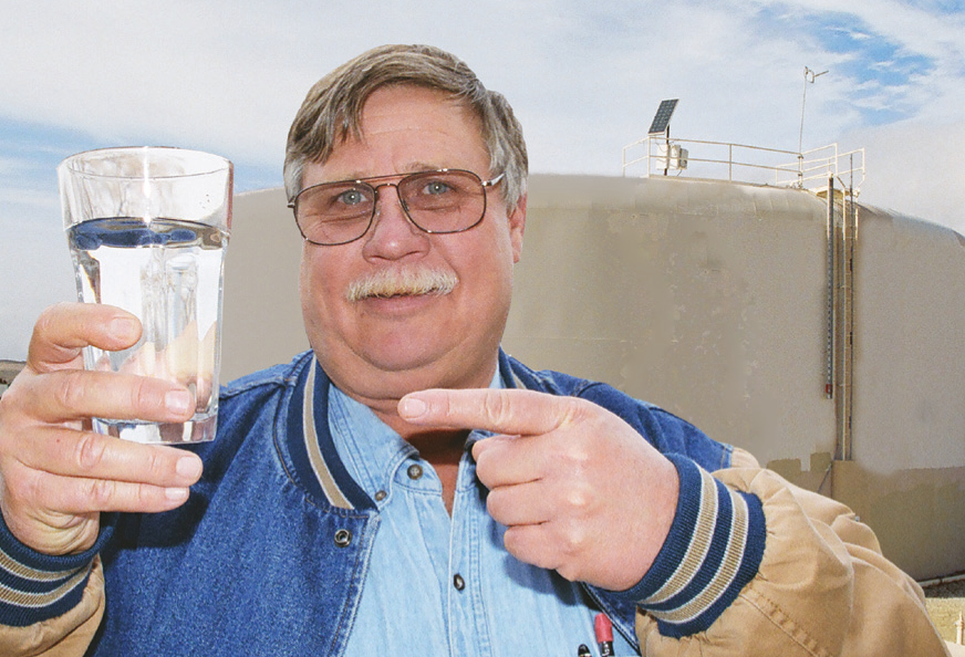 image showing happy water operator holding clear glass of water with a potable water tank in the background